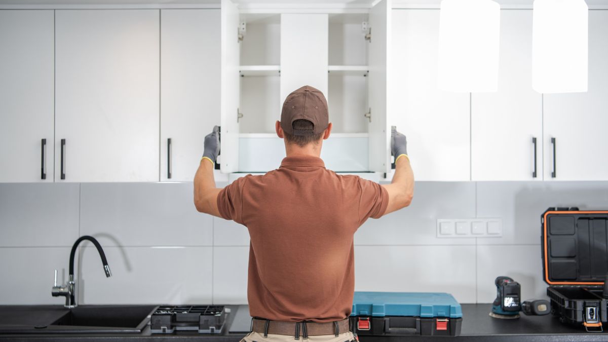 In a kitchen, a man dressed in a brown shirt stands, engaged in a culinary task amidst kitchenware.